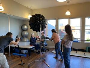 Camera crew taking photos of a woman lifting weights with a trainer for a senior living photo shoot.