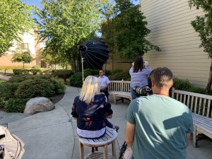 Looking over the shoulder of the cameraman during an interview of a man sitting on a bench during a senior living photo shoot.