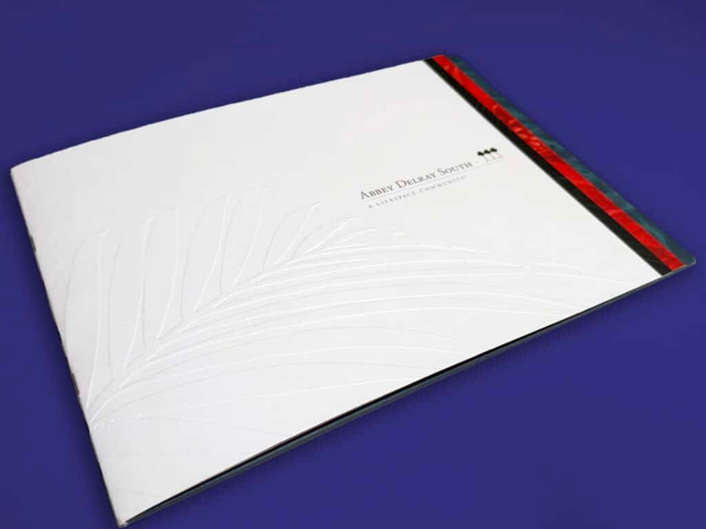 A white booklet with a subtle leaf pattern and a red-green edge rests on a blue background.